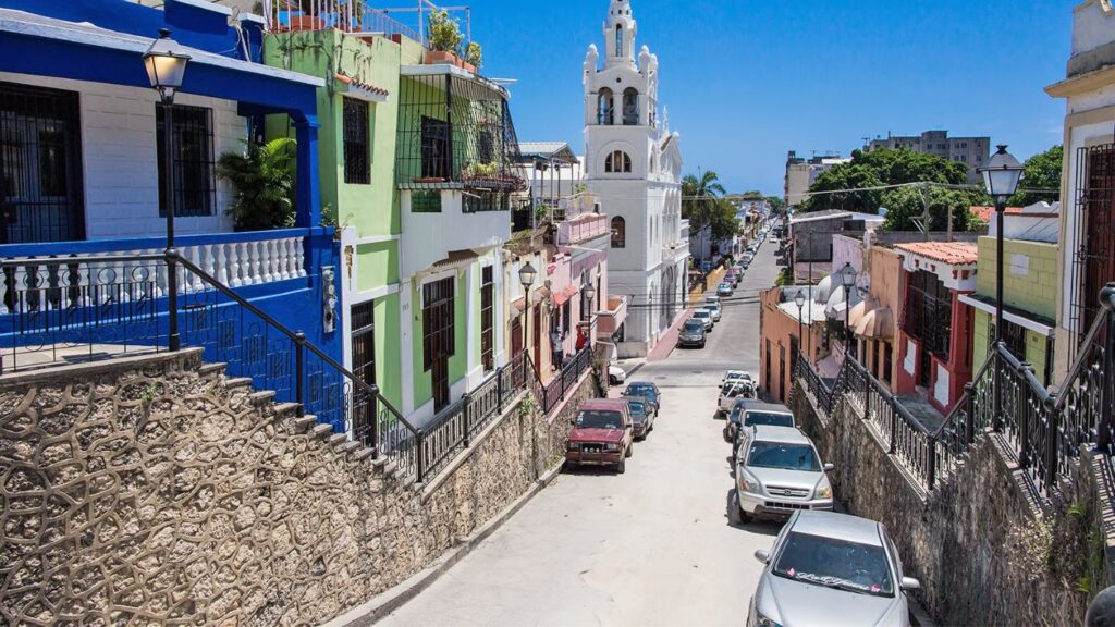 calle en Santo Domingo, República Dominicana. Torre, casas de colores, vehículos aparcados